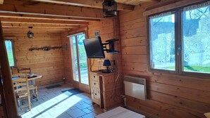 A wooden cabin with a TV, a small table, and a window with lace curtains.