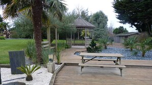 A wooden deck with a picnic table, surrounded by a garden with palm trees and a gazebo. - country house in Plestin les Grèves (Plestin-Les-Grèves)
