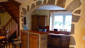 A kitchen with a stone archway, wooden cabinets, a bar area with stools, and a window providing natural light. - country house in Plestin les Grèves (Plestin-Les-Grèves)