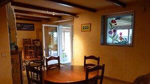A dining area with a wooden table and chairs, a window with a flower painting, and a door leading outside. - country house in Plestin les Grèves (Plestin-Les-Grèves)