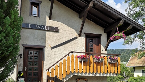 A building with a sign reading "LE WALIS" and a wooden staircase leading to a balcony with hanging flower baskets. - Chartreuse Natural Park: cozy nest at the start of hiking trails! (Le Sappey-En-Chartreuse)