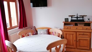 A cozy room with a wooden dining table, chairs, a television, and a wooden cabinet with a scale. - Chartreuse Natural Park: cozy nest at the start of hiking trails! (Le Sappey-En-Chartreuse)