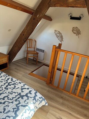 Une chambre avec un plafond en pente, des poutres en bois, un lit recouvert d’une couvre-lit à motifs, une chaise, un radiateur et des œuvres d’art mural.