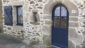 A stone building with a dark blue door and windows, featuring a number plaque and a small window with a diamond-shaped decoration.