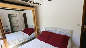 Une chambre avec deux lits, un grand miroir, un luminaire suspendu et une porte.