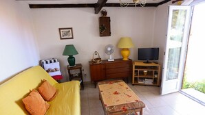 Un salon chaleureux avec un canapé jaune, une table basse en bois, un téléviseur et une porte-fenêtre coulissante donnant sur un espace extérieur.
