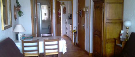 Een eethoek met een tafel en stoelen, een houten kast, en een keuken op de achtergrond.