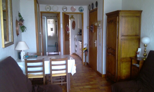 Un comedor con mesa y sillas, un armario de madera y una cocina al fondo.