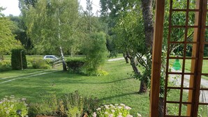 Un jardin avec un sentier, des jardinières en bois ornées de fleurs et une voiture garée au fond.