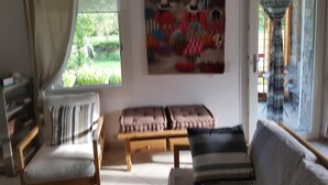 Un salon avec un canapé, un banc, un fauteuil, un tableau et une fenêtre avec des rideaux.