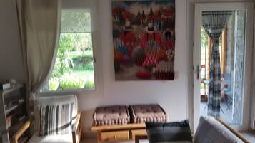 Un salon avec un canapé, un banc, un fauteuil, un tableau et une fenêtre avec des rideaux.