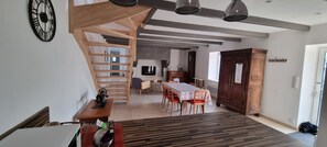 Relax in this open living area with a high ceiling, featuring a dining table for four, comfortable chairs, and a mounted television.
