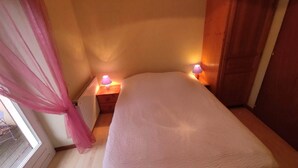 Ein Schlafzimmer mit einem Bett, zwei Nachttischlampen, einem Heizkörper, einem Fenster mit Vorhängen und einem Holzschrank.