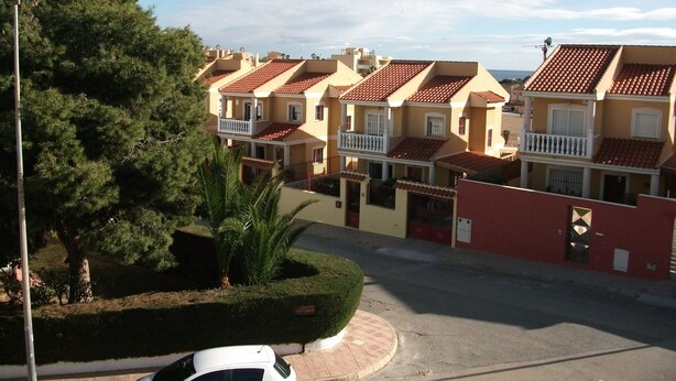 Calle residencial con casas adosadas, un coche blanco estacionado en la banquina y un seto bien cuidado.