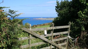 A wooden gate with a sign, overlooking a coastal landscape with greenery and the sea.