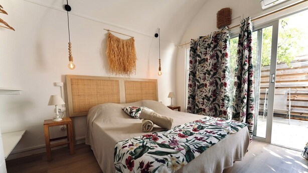 Un dormitorio con cama, mesita de noche, lámpara, cabecera de mimbre y vistas al exterior a través de una puerta de cristal.
