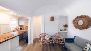 Un espacio habitable compacto con cocina, dos sillas de mimbre, un sofá y un espejo decorativo.