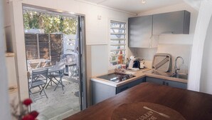 Una cocina compacta con estufa integrada, un lavamanos y una pequeña encimera. Se ve un comedor con una mesa y sillas a través de la puerta de cristal.