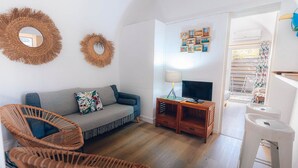 Una sala de estar acogedora con un sofá, dos sillones de mimbre, una mesita de madera con una lámpara y un televisor.
