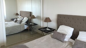 Ein Hotelzimmer mit einem großen Bett, zwei Nachttischen, einem Spiegel und einem gepolsterten Kopfteil.