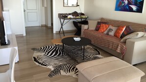 Ein modernes Wohnzimmer mit einer Couch, einem zebra-gemusterten Teppich, einem kleinen runden Tisch und einem Schreibtisch mit Stuhl.