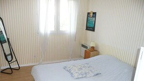 Een slaapkamer met een bed, nachtkastje, lamp en raam met gordijnen.