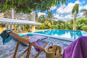 A pool area with a lounge chair, a table, and a hanging hammock. - Mabouya (Le Diamant)