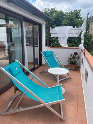 Un balcon avec deux chaises longues et une petite table, un pot de fleurs et une vue sur la verdure.