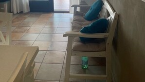 A room with a sofa, a table, a chair, a small shelf, a wall-mounted lamp, and a sliding glass door leading to an outdoor area.