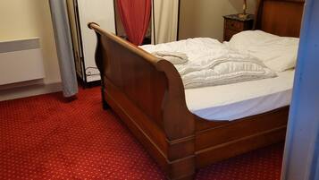 A bedroom with a wooden bed, red carpet, and a small bedside table with a lamp.