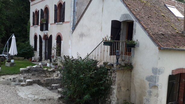 Un edificio con fachada de piedra, varias ventanas con contraventanas, un balcón pequeño con barandilla y una escalera que conduce a la entrada.