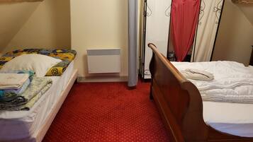 A small, cozy room with two single beds, a red patterned carpet, a white radiator, and a window with curtains.