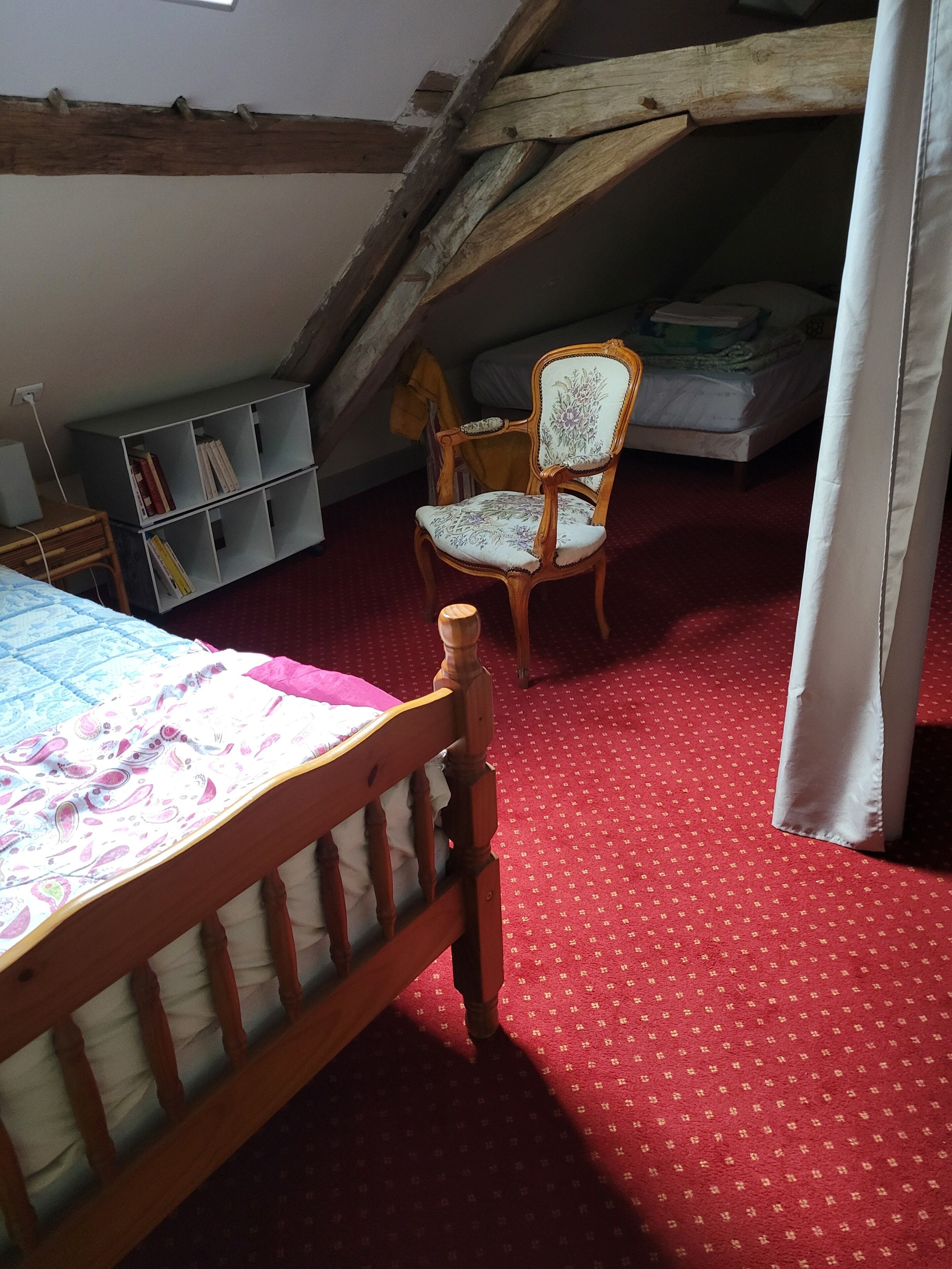 Een slaapkamer met een houten bed, een rode vloerkleed, een houten stoel, een boekenkast en een matras op de vloer.