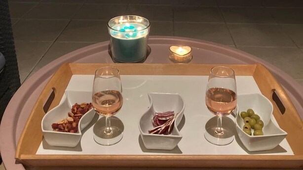 Escena junto a la piscina con una bandeja de aperitivos y bebidas, una vela y una piscina iluminada en la noche.