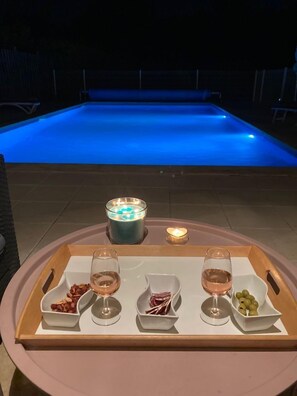 A poolside setting with a tray of snacks and drinks, a candle, and a glowing pool at night. - 4-bedroom villa with heated private pool and large enclosed garden in Lourmarin (Lourmarin)