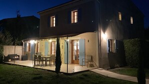 Una casa de dos pisos con un patio, una mesa de comedor y sillas.