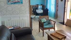 A living room with a black leather sofa, a wooden coffee table, and a blue chair. There is a dining area with a table and chairs in the background. - New: ground floor house, quiet location, close to the sea (Riantec)
