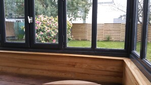 A room with a large window, wooden bench, and a view of a garden with a wooden fence and flowering plants. - New: ground floor house, quiet location, close to the sea (Riantec)