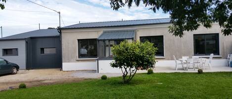 A modern house with a fenced yard, a small tree, and outdoor furniture.