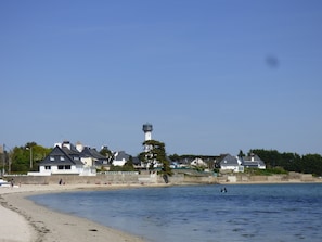 A coastal scene with a lighthouse, beach, and residential buildings.