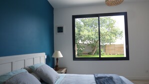 A bedroom with a large window, a bed with patterned bedding, a bedside lamp, and a wall-mounted picture. - New: ground floor house, quiet location, close to the sea (Riantec)