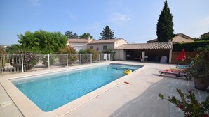 A rectangular swimming pool with a tiled deck, surrounded by a white fence, and a small garden area with potted plants and a red umbrella. - Mazan holiday villa with private swimming pool on 3000m (Mazan)