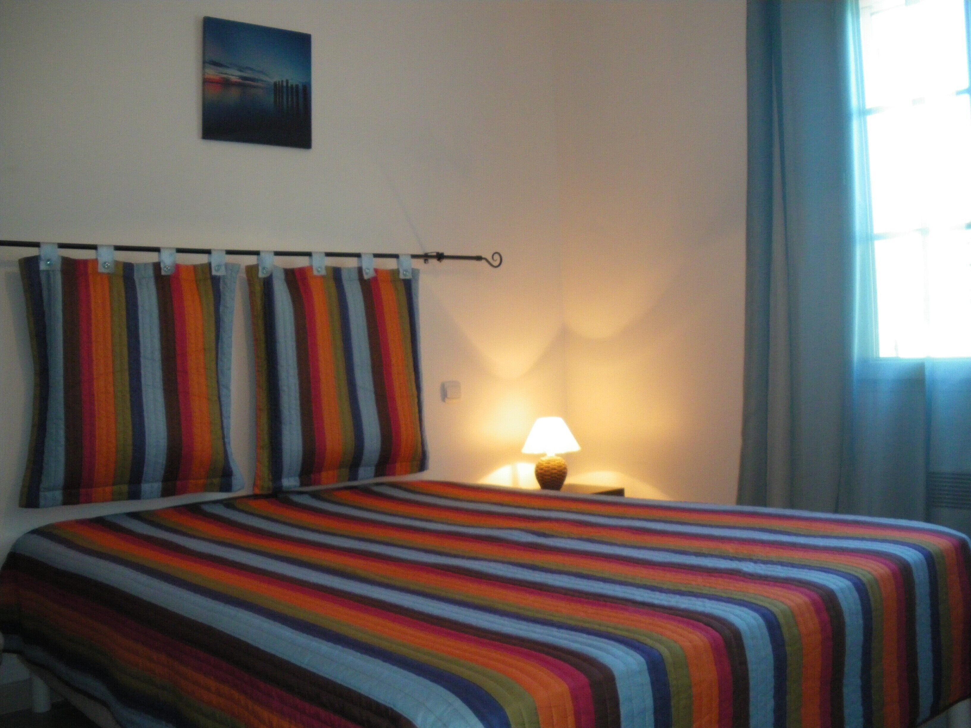Una habitació d'hotel amb un llit, una tauleta de nit, una làmpada i una finestra amb cortines.