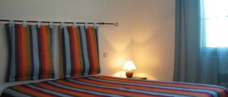 Una habitació d'hotel amb un llit, una tauleta de nit, una làmpada i una finestra amb cortines.