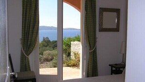 Une chambre avec un lit, une chaise et une vue sur la mer, visible à travers une porte vitrée.