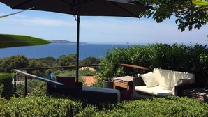 Une terrasse avec des meubles d’extérieur, un grand parasol et une vue sur la mer.
