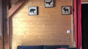 A dark blue sofa with two red cushions, wooden walls with animal-themed wall art, and a red curtain. - CHALET SUR FLANC DE COLLINE A BESSE PROMO last minute in May (Besse-Et-Saint-Anastaise)