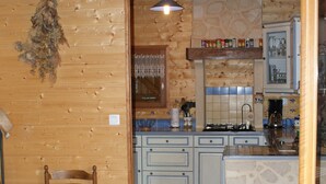 A rustic kitchen with wooden walls, a stone island, and a dining area with a wooden table and chairs. - CHALET SUR FLANC DE COLLINE A BESSE PROMO last minute in May (Besse-Et-Saint-Anastaise)