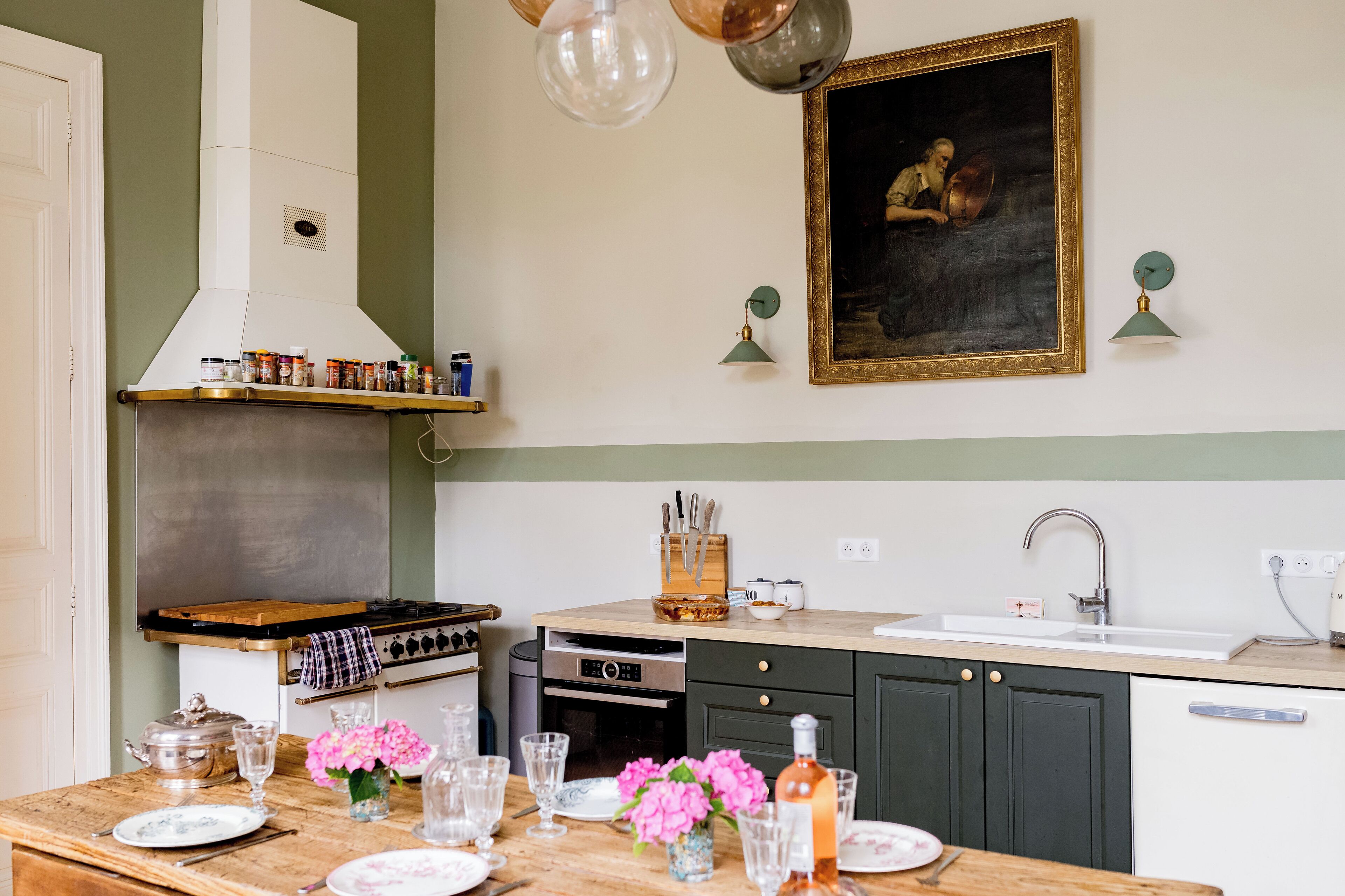 A kitchen with a stove, oven, sink, and a painting on the wall.