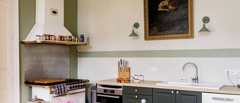 A kitchen with a stove, oven, sink, and a painting on the wall.